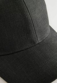 Black cap made of textured fabric. Features a rounded crown and a stiff brim, with visible stitching along the seams.