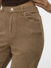 Kord hlače svetlo rjave barve z reliefno rebrasto tkanino, sprednjim žepom in kovinskim gumbom za zapiranje. Prilegajoč se model z visokim pasom.