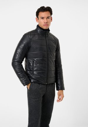 Zwarte leren pufferjack met hoge kraag, horizontaal gestikte patroon, voorkant met rits en zijzakken. Draag over grijze broek.