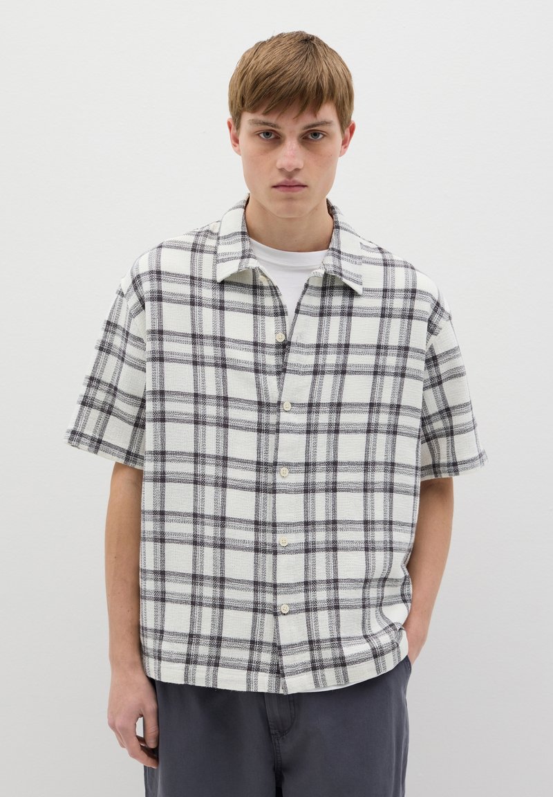 Chemise à manches courtes en carreaux blancs et noirs, avec une fermeture à boutons sur le devant et un col décontracté, dotée d'un tissu texturé.