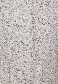 Měkká textura šedé a bílé bouclé tkaniny se švem probíhajícím vertikálně středem.