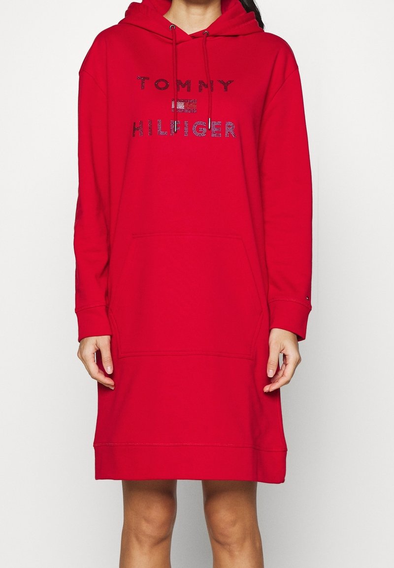 Personne portant une robe à capuche rouge longueur genou avec une poche avant et le texte et logo "Tommy Hilfiger" sur la poitrine.