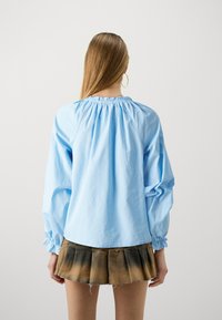 Svijetloplava bluza dugih rukava s napučenim dekolteom i elastičnim manžetama, u kombinaciji s kratkom, plisiranom, ombre traper suknjom.