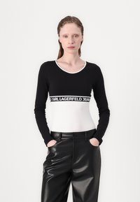 Black and white long-sleeve top featuring a round neckline and a contrasting waistband with "KARL LAGERFELD JEANS" branding. Paired with black leather pants.