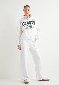 Sudadera blanca con gráfico de "Atlantic City" en negro, combinada con pantalones anchos blancos. Ambos tienen una textura suave y un corte relajado.