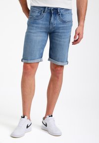 Leren denim shorts in lichtblauw met opgerolde zoom, uitgerust met een knoopsluiting, voor- en achterzakken, gecombineerd met witte sneakers.