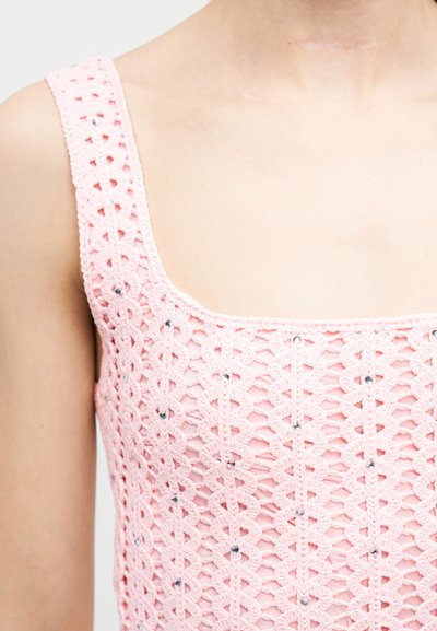 Gros plan sur une personne portant un haut rose au crochet avec des accents en strass sur les bretelles et le devant.