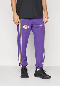 Lilla Nike joggingbukser med hvide og gule side-striber, der har et Los Angeles Lakers-logo på venstre lår. Struktureret stof med en afslappet pasform.