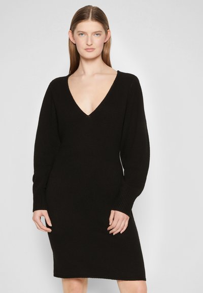 Vestido preto de malha com um decote em V profundo, mangas longas ajustadas e corte reto. O tecido é texturizado e elástico, proporcionando um ajuste justo.