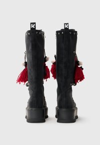 Stivali neri al ginocchio con finitura opaca, hardware argentato, nappine rosse e una suola nera spessa. Presentano borchie decorative e catene.