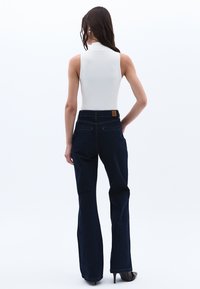 Valkoinen hihaton body, joka on yhdistetty tummansinisiin leveisiin denim-housuihin, joissa on takataskut ja teksturoitu vyötärö. Mustat korkokengät.