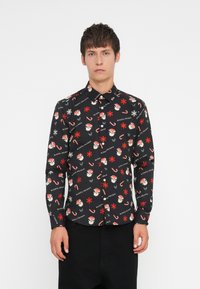Chemise noire à boutonnière avec un motif festif répétitif comprenant des visages de Santa, des cannes en sucre d'orge, des flocons de neige et le texte "JOURS DE FÊTES HEUREUX".