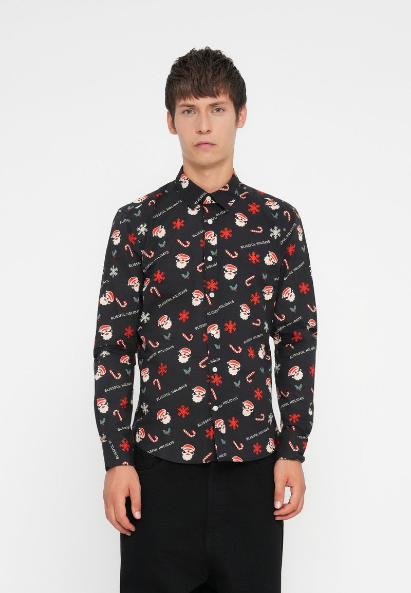 Chemise noire à boutonnière avec un motif festif répétitif comprenant des visages de Santa, des cannes en sucre d'orge, des flocons de neige et le texte "JOURS DE FÊTES HEUREUX".