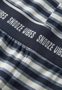 Bomullsbokser med en marineblå elastisk linning med teksten "SNOOZE VIBES." Stripete mønster i ulike nyanser av blått og hvitt.