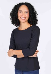 Black three-quarter sleeve top made of smooth fabric, featuring a round neckline and relaxed fit, paired with blue denim jeans.