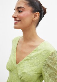 Hellgrünes Kleid mit floralem Stickerei, V-Ausschnitt und durchscheinenden langen Ärmeln. Verfügt über einen strukturierten Stoff und Raffung im Brustbereich.