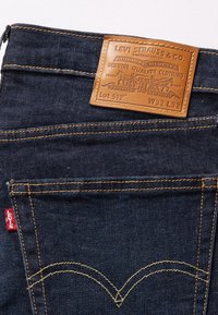 Poche arrière de jean Levi's bleu foncé avec surpiqûres orange et un patch en cuir marron affichant la marque et la taille W32 L32.