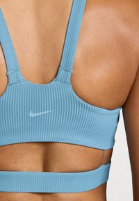 Top sportivo azzurro chiaro a coste con schiena curva, bretelle strette e un discreto logo Nike. La texture appare liscia con un design aderente.