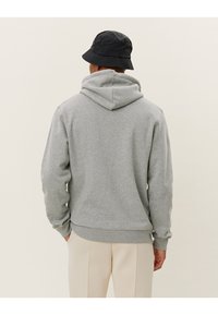 Gray hoodie featuring a drawstring hood and ribbed cuffs, worn with light-colored pants and a black bucket hat. Rear view, plain background.