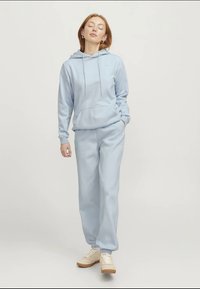 Jasnoniebieska bluza z kapturem i pasujące dresy z miękkiego materiału, z przednią kieszenią i sznurkiem w kapturze, w połączeniu z kremowymi trampkami.