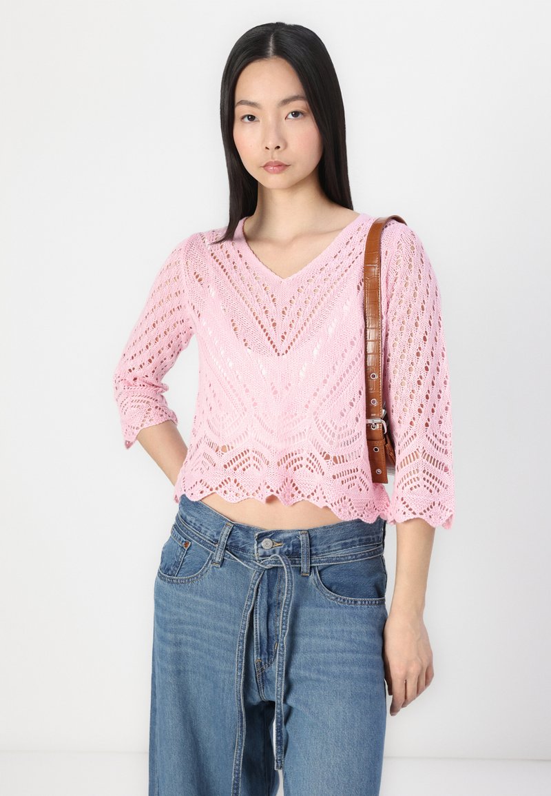 Top court en tricot rose avec un décolleté en V, doté d'un motif en dentelle, de manches trois-quarts et de bords festonnés, assorti à un jean taille haute bleu clair.