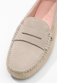 Mocassin en suède beige avec un détail de couture sur le devant et un bord crème contrastant. Texture douce et semelle intérieure rose.