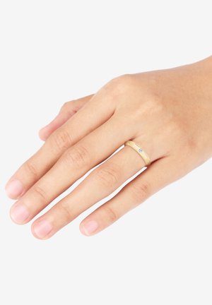 Guldtonet ring med en glat, rund skæft og en lille, klar ædelsten som accent. Vist på en hånd med naturlige negle.