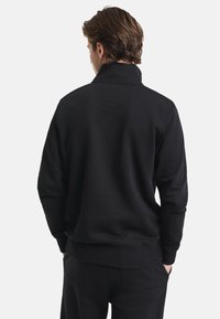 Black sweatshirt with high collar, long sleeves, and a relaxed fit. Smooth texture with ribbed cuffs and hem. Hidden seam detail at the neck.