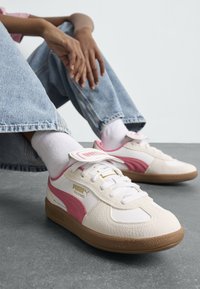 Baskets blanches avec des accents roses, tige en cuir texturé, bout rond, fermeture lacée et semelle en caoutchouc gomme. Comprend une languette rembourrée.