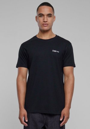 Sort kortærmet t-shirt med rund halsudskæring, der har hvid tekst "Deja vu" på venstre brystområde. Stoffet ser glat ud.