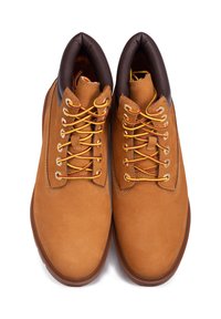 Une paire de bottes de travail en cuir beige avec des lacets jaunes et rouges, des cols rembourrés marron et des semelles en caoutchouc marron sur un fond blanc.