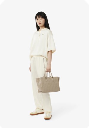 Chemise beige clair à col rond et pantalon assorti, accompagnés d'un sac à main texturé marron clair. Les sneakers sont crème et marron.