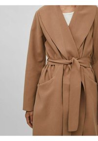 Manteau portefeuille marron avec un large col, ceinture à la taille et deux poches avant. Fabriqué en tissu doux et texturé, il présente un design simple.