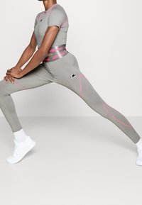 Sportovní oblečení přiléhavého střihu v šedé barvě s růžovými detaily. Krátký rukáv u topu a legíny s vysokým pasem. Obsahuje logo a pružný materiál.