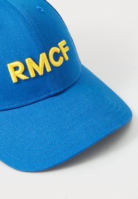 Kék sapka sárga "RMCF" hímzéssel, struktúrált koronával és ívelt napellenzővel. Texturált anyagból készült, látható varrással.