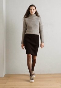 Maglione a collo alto grigio a coste, gonna nera aderente, collant scuri e sneakers chiare con dettagli metallici. Design semplice e lineare.
