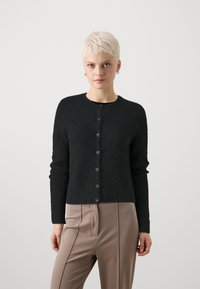 Μαύρος, υφασμένος cardigan με μακριά μανίκια, στρογγυλή λαιμόκοψη και έξι κουμπιά, συνδυασμένο με ανοιχτό καφέ, πλισέ παντελόνι.