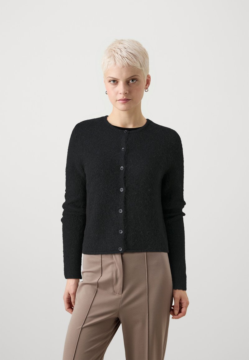 Μαύρος, υφασμένος cardigan με μακριά μανίκια, στρογγυλή λαιμόκοψη και έξι κουμπιά, συνδυασμένο με ανοιχτό καφέ, πλισέ παντελόνι.