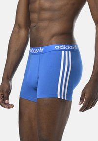 Blaue sportliche Boxershorts aus glattem Stoff, mit einem weißen Bund, der das "adidas"-Logo und drei weiße Streifen an den Seiten trägt.