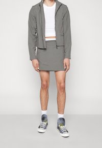 Giacca grigia chiara con un design cropped, abbinata a una mini gonna coordinata. Calzature con sneaker grigie e bianche con accenti neon.
