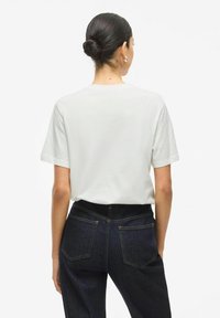 Vit t-shirt med kort ärm och avslappnad passform, kombinerad med mörkblå denimjeans med bakfickor och synliga sömnadsdetaljer.