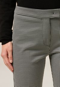 Zwart-witte houndstooth-gepatroneerde broeken met een gladde textuur, voorzien van een platte tailleband en zijzakken.