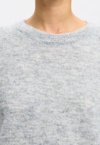 Hellgrauer Pullover mit einer weichen, strukturierten Oberfläche. Verfügt über einen runden Halsausschnitt und gerippte Manschetten. Das Material wirkt flauschig mit einem dezenten Muster.