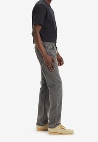 Grå denimjeans med rak passform, bärs med en svart t-shirt med kort ärm och beige mockastilskor, som har en avslappnad passform.