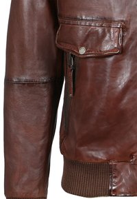 Chaqueta bomber de cuero marrón con dobladillo de punto acanalado, bolsillo lateral con cremallera y un brillo sutil. Presenta detalles de costura en las mangas.