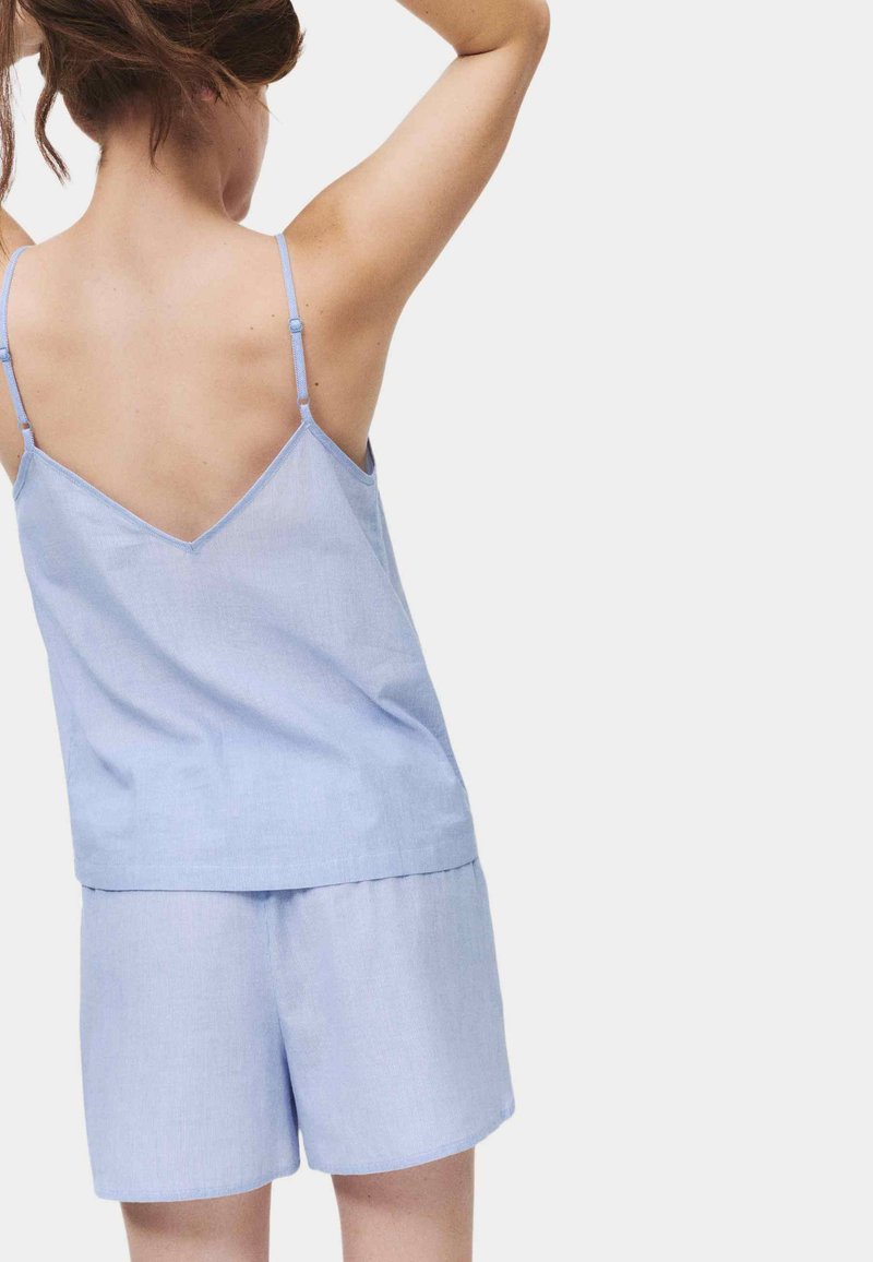 Woman wearing light blue sleeveless top and matching shorts, shown from the back with arms raised against a plain background.