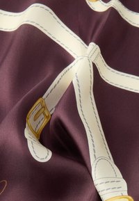 Hedvábná látka v tmavě fialové barvě s krémovými pásky se žlutými přezkami a světle šedým prošíváním, vytvářející detailní vzorovaný design.