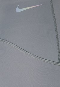 Tessuto atletico grigio con una texture liscia, cuciture curved e un logo Nike riflettente nei toni di blu pallido e rosa.