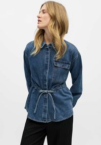 Denim krekls ar garām piedurknēm, regulējamu stringu vidukli, apkakli un krūšu kabatu. Ar vidēju zilo mazgāšanu un strukturētu piegriezumu.