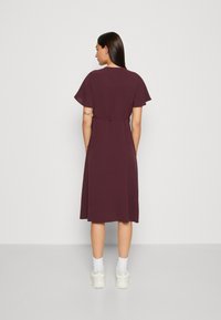 Burgundy dress with short flutter sleeves, belted waist, and knee-length skirt. Smooth texture and lightweight fabric.